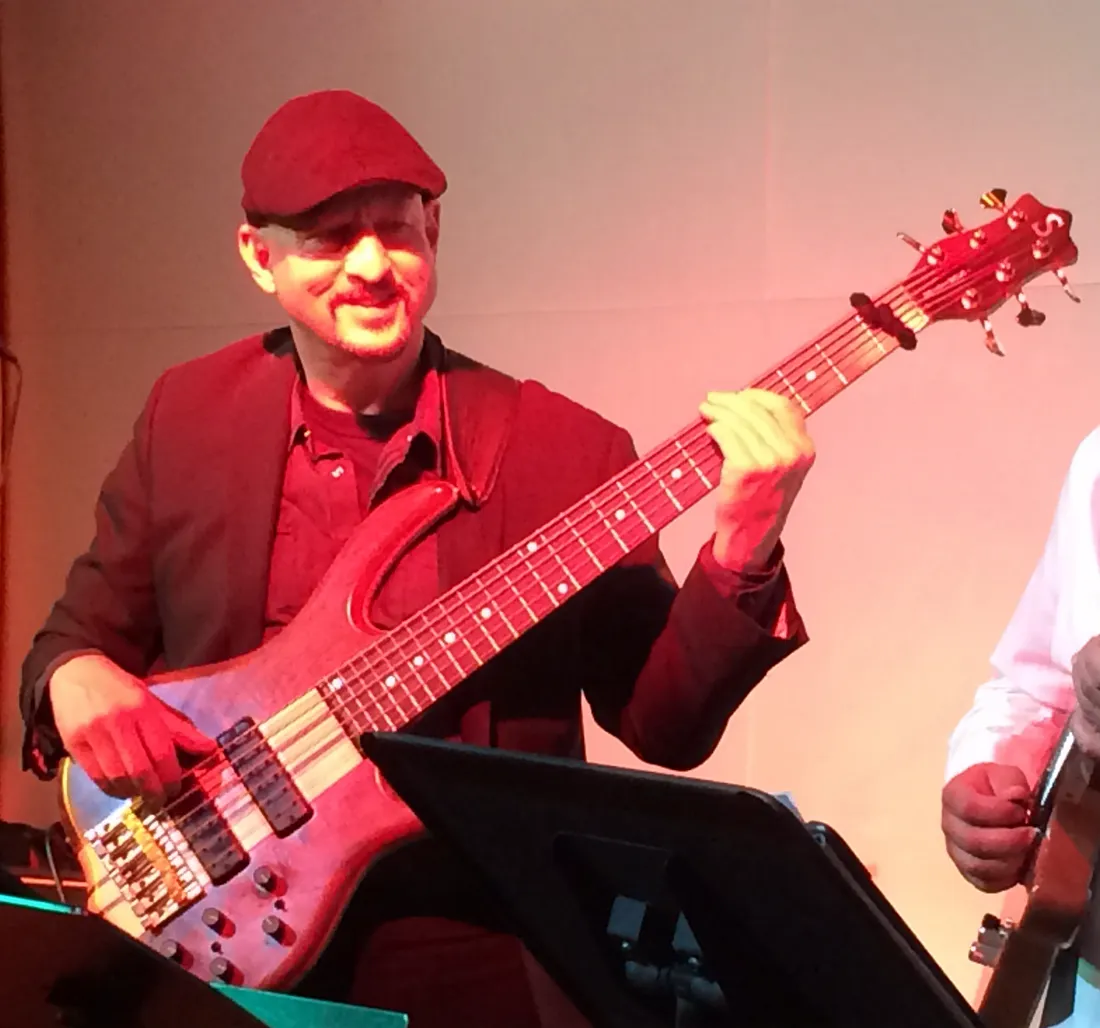 Russ Rodgers playing bass at a club gig under warm red lighting
