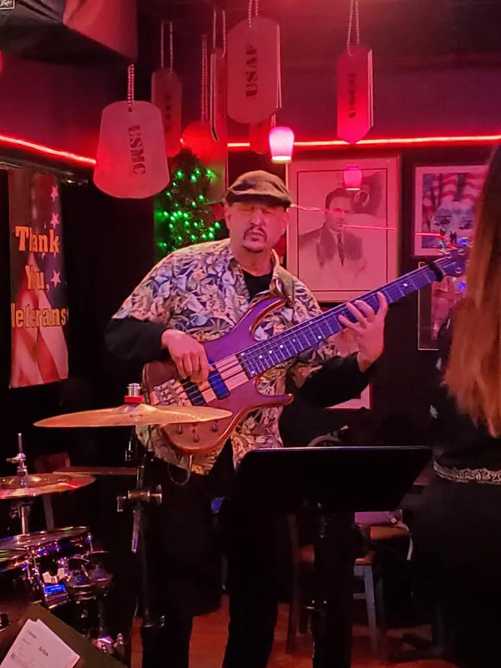Russ Rodgers in a Hawaiian shirt playing bass at a red-lit bar