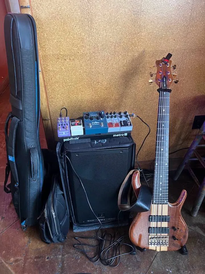 The full rig lined up for load-in — gig bag, backpack, powered speaker with the Metro board on top, and the six-string Ken Smith