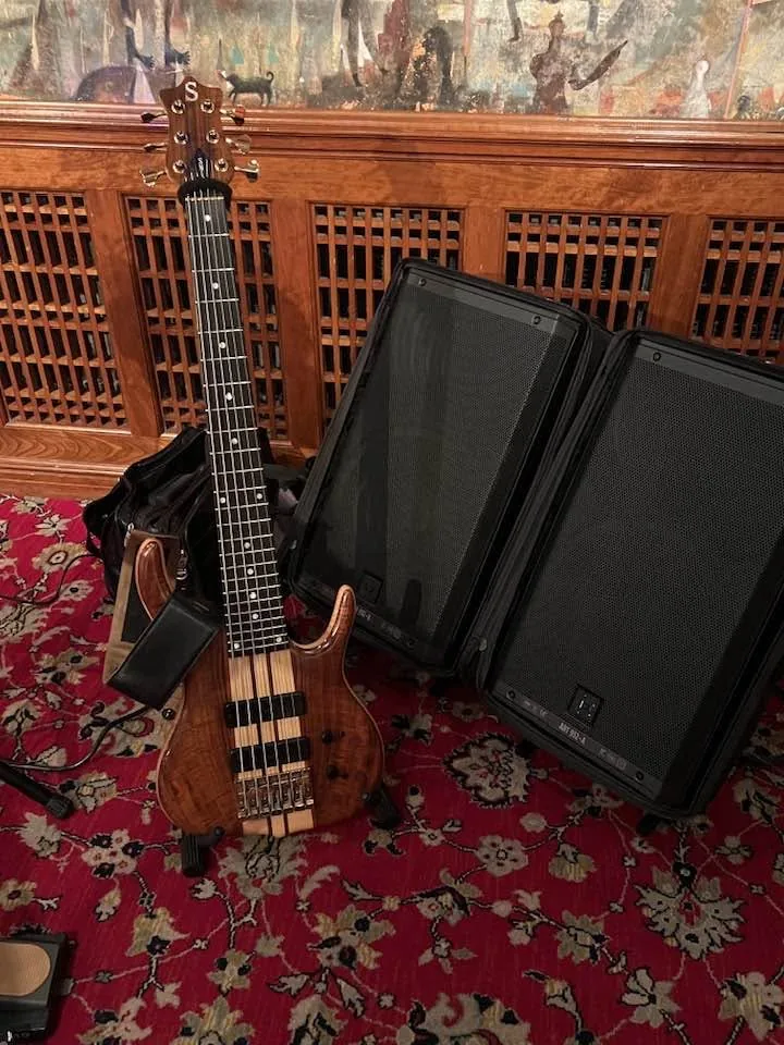 Russ's six-string Ken Smith on a stand beside two RCF powered speakers in an ornate venue