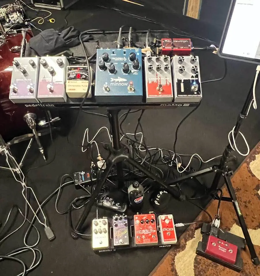 Full stage setup at a gig: the Metro board on its stand, the Nano effects board and the AirTurn page turner on the floor, drums behind