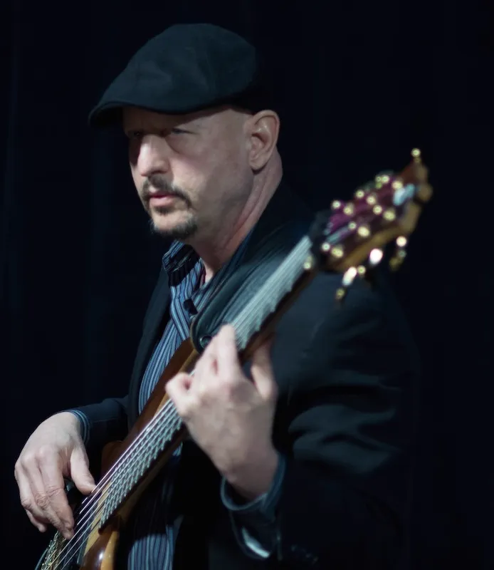 Russ Rodgers in a dark suit playing bass on stage