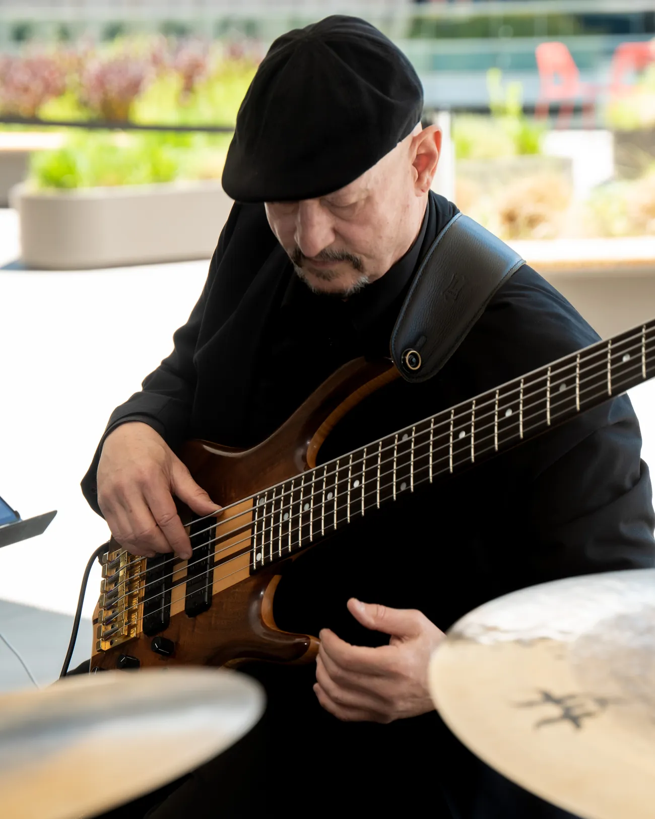 Russ Rodgers playing his six-string bass guitar, seated between two cymbals at an outdoor event
